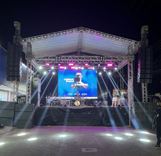 Grande palco de rua montado à noite pela GDX Brasil, com estrutura de treliças, cobertura, line arrays de som e iluminação de palco durante um festival.